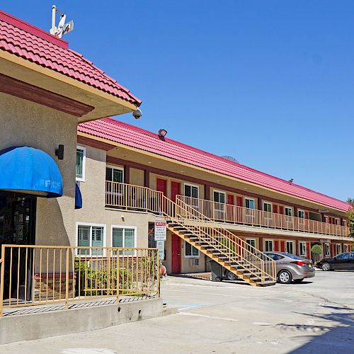 The image shows a motel with a red roof and blue awnings, a two-story structure with outdoor staircases, a parking lot, and palm trees in the background.