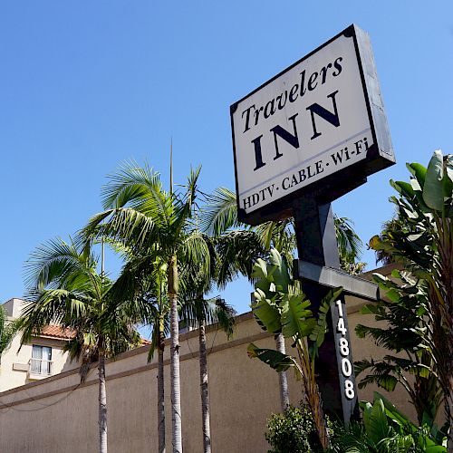 The image shows a sign for Travelers Inn, offering HDTV, cable, and Wi-Fi, surrounded by palm trees and a building with the address 14808.