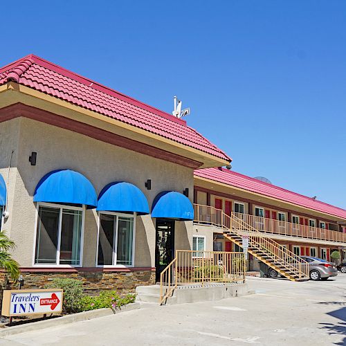 This image shows the exterior of a two-story motel with blue awnings, a red roof, and a parking area with some cars in front.