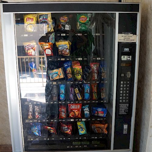 This image shows a vending machine filled with various snacks and drinks, featuring a keypad and coin slot on the right side.