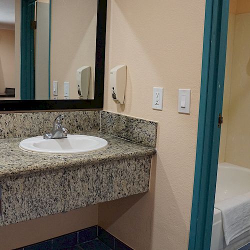 The image shows a bathroom with a granite countertop, sink, mirror, over-sink lighting, bathtub with shower curtain, and a toilet.