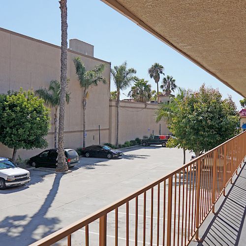 The image shows a motel with a parking lot, lined with several cars, palm trees, and a second-floor walkway railing along the right side.