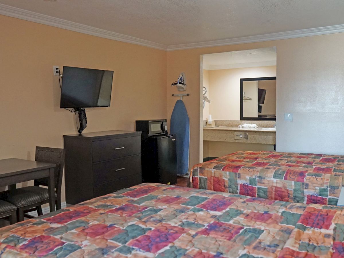 A hotel room featuring two beds, a table with chairs, a TV, a microwave, an iron with an ironing board, and an open bathroom view ending the sentence.