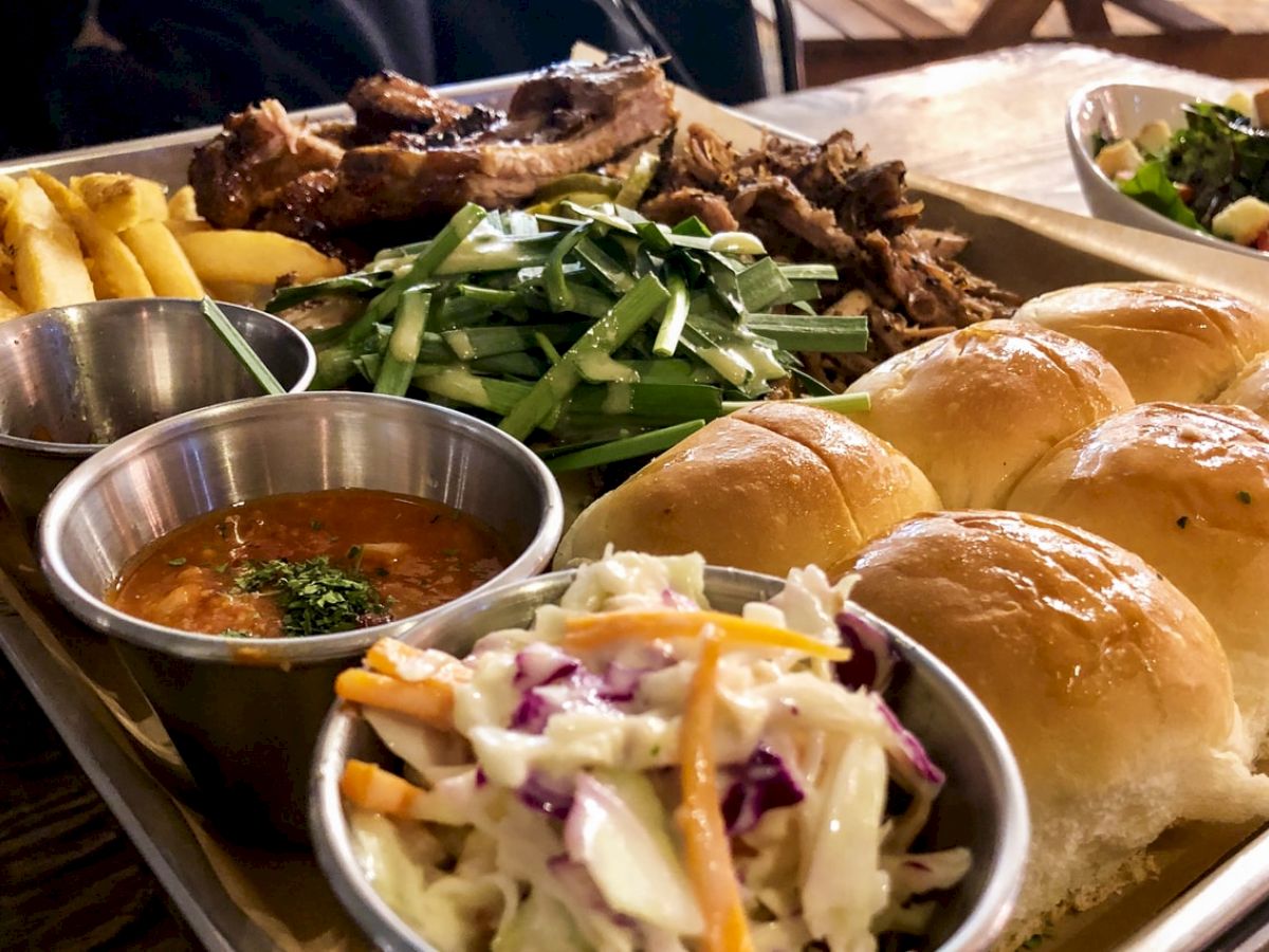 The image shows a food platter with buns, coleslaw, French fries, meat, a bowl of sauce, and a mixed vegetable salad on the side.