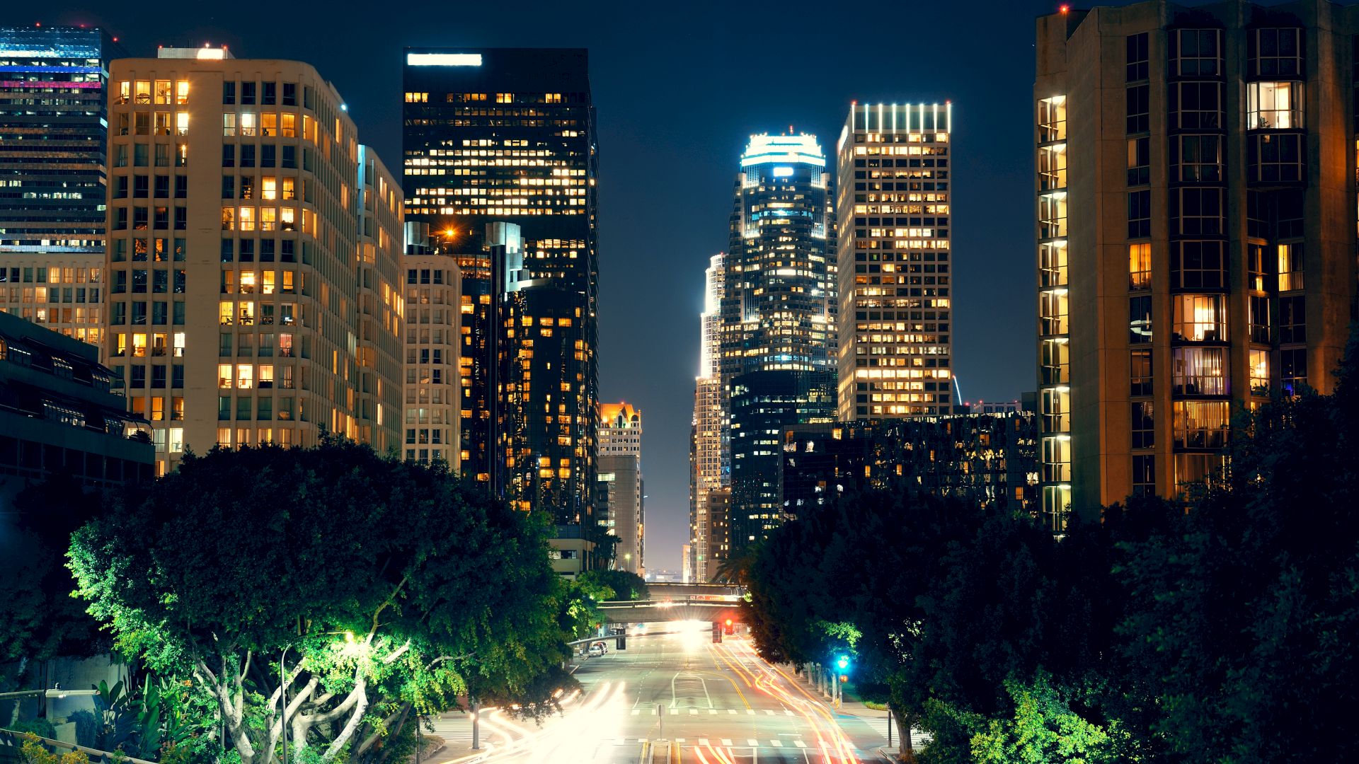 The image shows a cityscape at night with tall, illuminated buildings and a street below with streaks of light from moving vehicles.