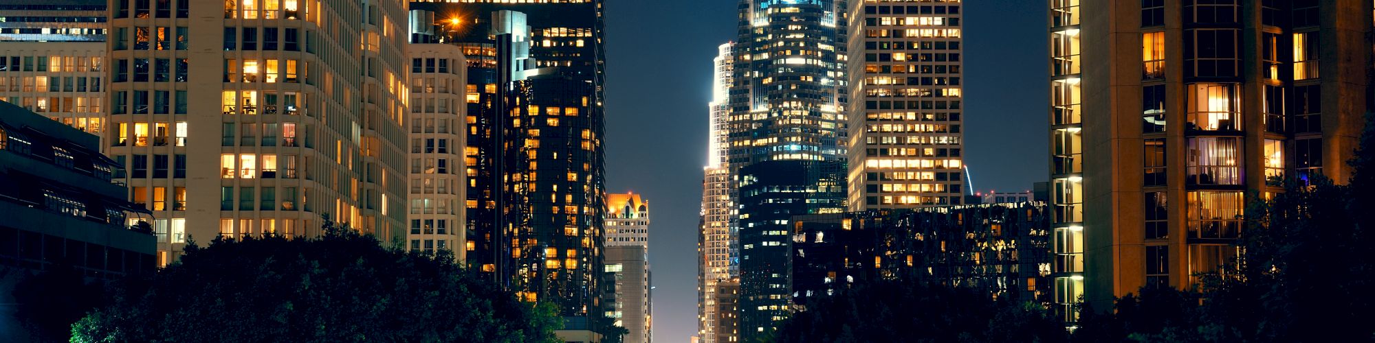 The image shows a cityscape at night with tall, illuminated buildings and a street below with streaks of light from moving vehicles.