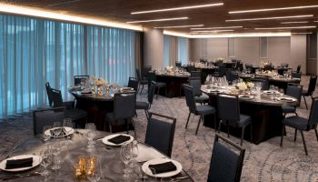 The image features an elegantly set dining hall with multiple round tables decorated with floral centerpieces and black napkins, ready for a formal event.