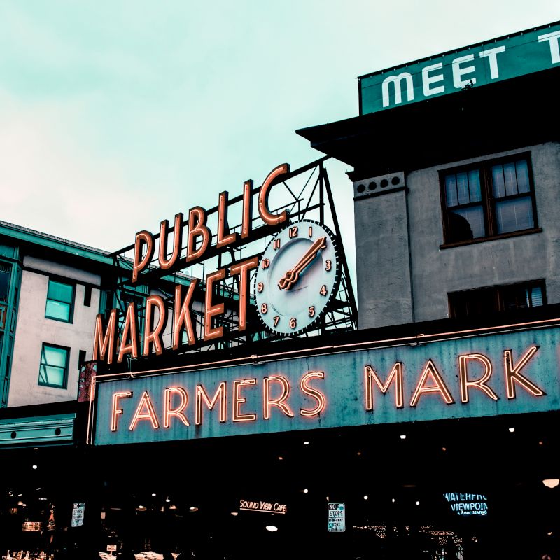 This image shows the iconic neon signs for a "Public Market" and "Farmers Market" with an old-fashioned clock, likely a popular urban market area.