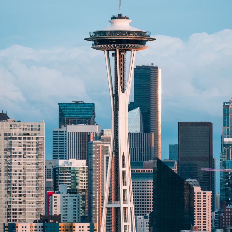 The image shows the iconic Space Needle in Seattle, Washington, with the city's downtown skyscrapers in the background, against a partly cloudy sky.