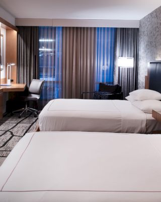 The image shows a modern hotel room with two neatly made beds, a wall-mounted TV, a desk with a chair, and contemporary decor ending the sentence.