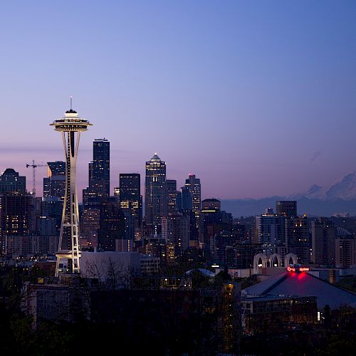 The image shows a city skyline at dusk with the Space Needle prominently in the foreground and Mount Rainier visible in the background.